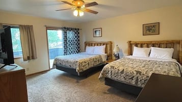 A hotel room with two beds, a ceiling fan, a television, and a window with curtains.