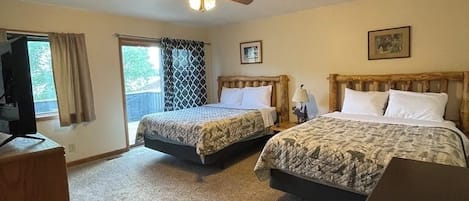 Habitación de hotel con dos camas, ventilador de techo, televisión y ventana con cortinas.