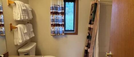 Une salle de bain avec des toilettes, un lavabo et une fenêtre avec des rideaux.