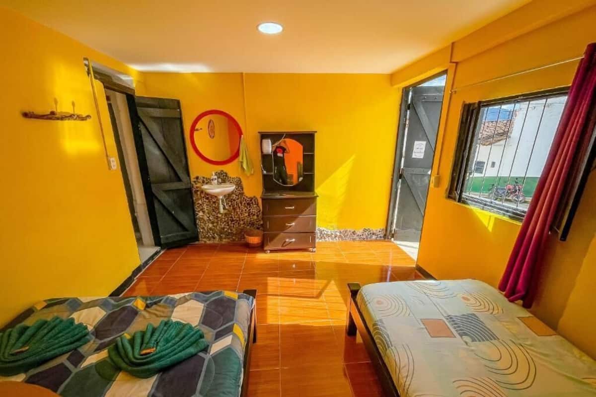 A room with two beds, a sink, a mirror, and a window with curtains.