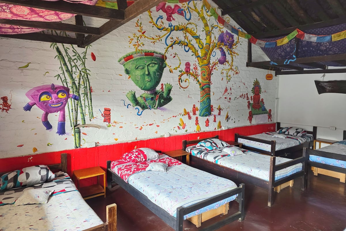 A dormitory room with four single beds, a mural on the wall, and a wooden ceiling.