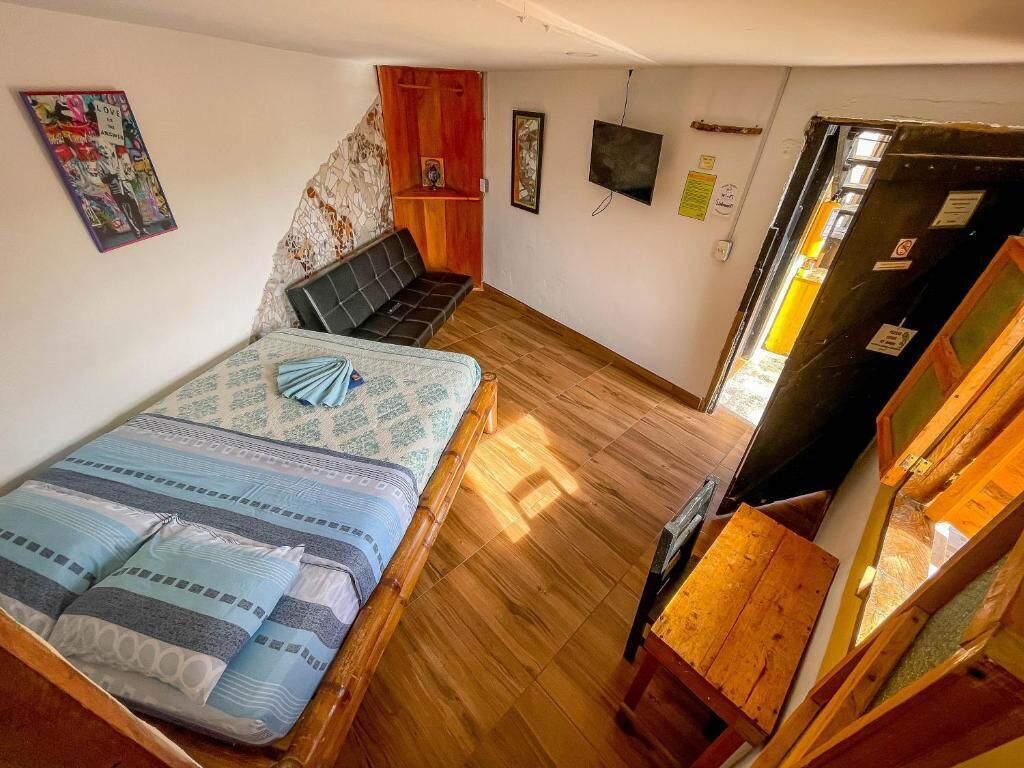 Una habitación pequeña con una cama, un banco de madera, un televisor y un refrigerador.