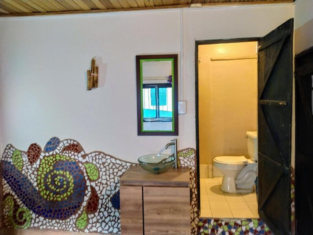 Une salle de bain avec un mur recouvert de mosaïques, un lavabo en verre, des toilettes et un miroir.