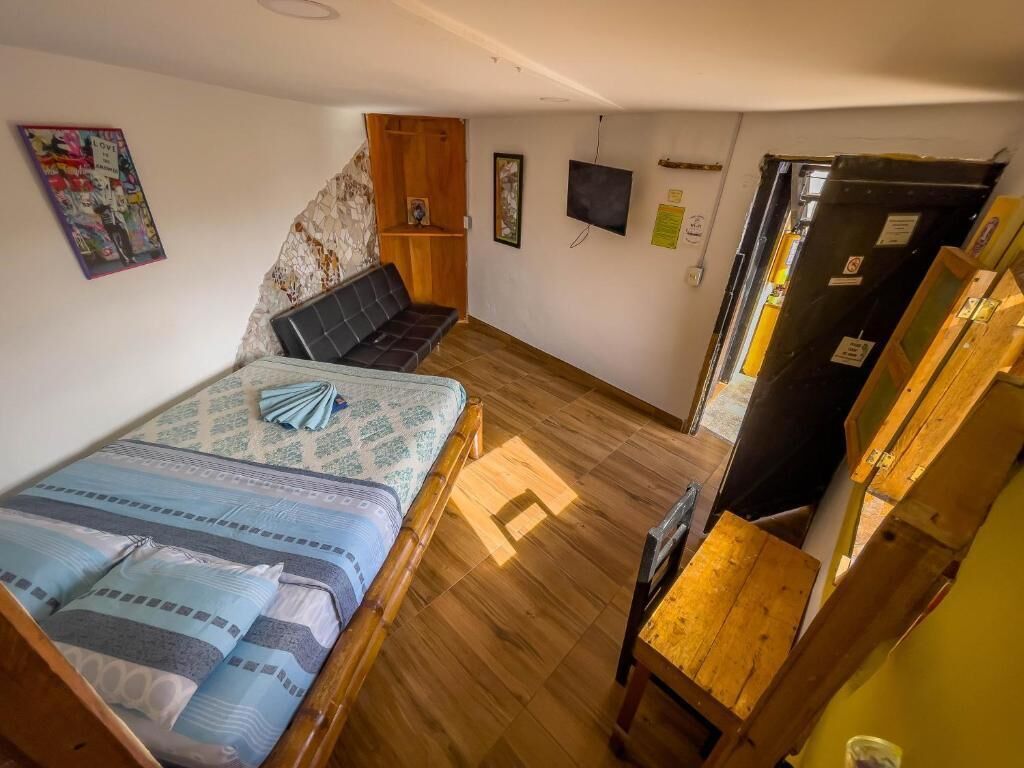 Una habitación con una cama, un banco de madera, un televisor y un refrigerador.