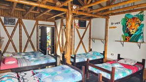 Ein Zimmer mit Bambus-Deckenbalken, mehreren Betten mit Blumenmuster-Bettwäsche, einem Spiegel und einer Wand mit einem Tiger-Mural.
