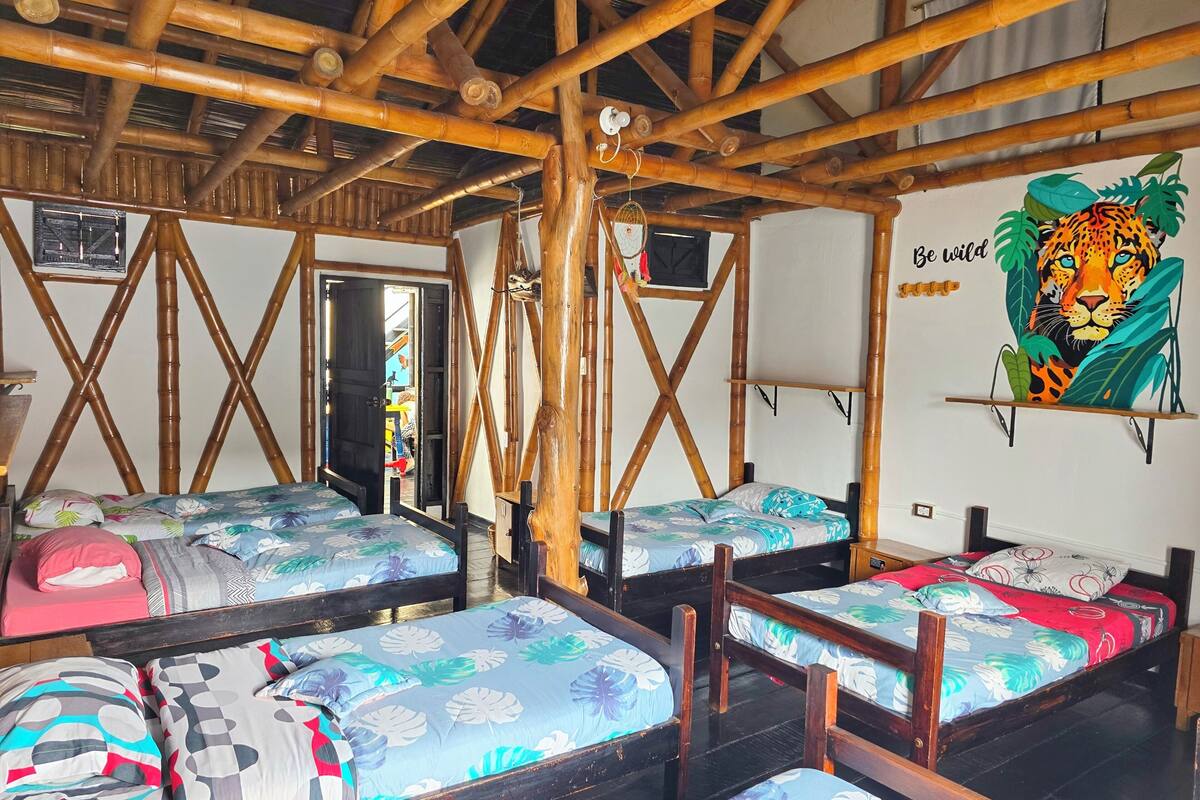 A room with bamboo ceiling beams, multiple beds with floral bedding, a mirror, and a wall with a tiger mural.