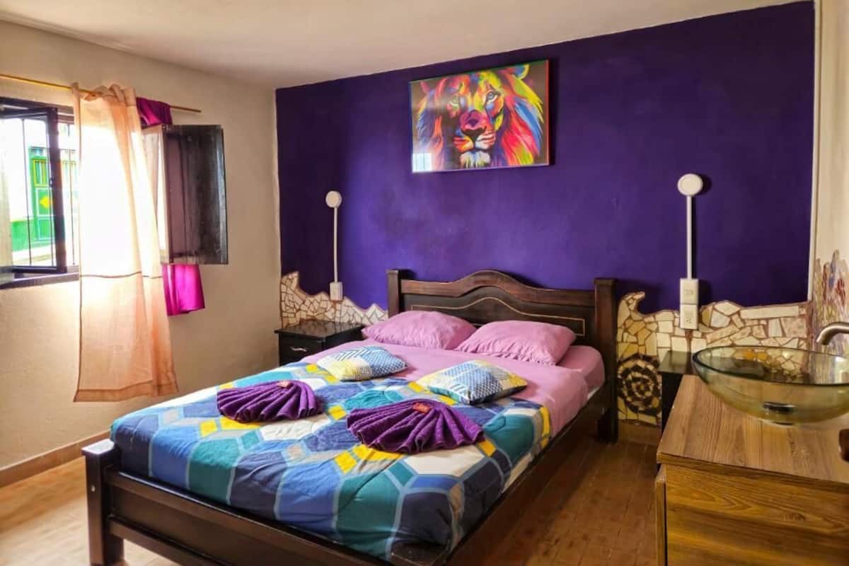 A bedroom with a bed, a painting, a nightstand, and a window with curtains.