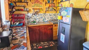 Eine Küche mit Fliesenboden, Holzschränken, einem Kühlschrank und verschiedenen Küchenutensilien auf Regalen.