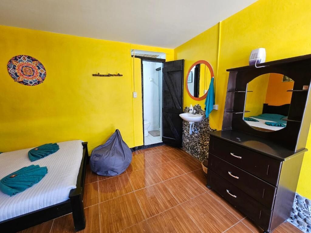 A room with a bed, a dresser, a mirror, a sink, and a door leading to another room.