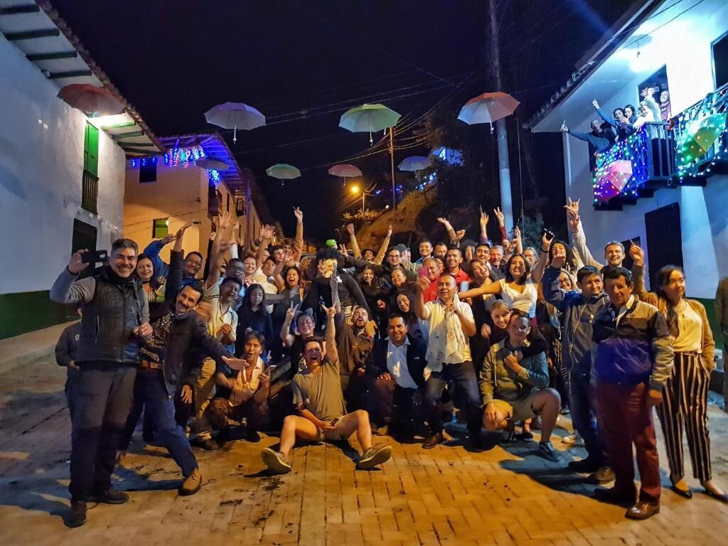 A group of people gathered in an outdoor area with a brick floor, under a covered structure with colorful lights.