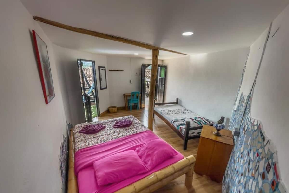 A room with a bed, a wooden bench, a small table, and a door leading to another room.
