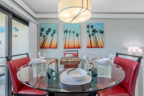 A dining area with a round glass table, red upholstered chairs, and a wooden centerpiece. - Santa Maria 1 #3205- Manatee Cove (Fort Myers Beach)