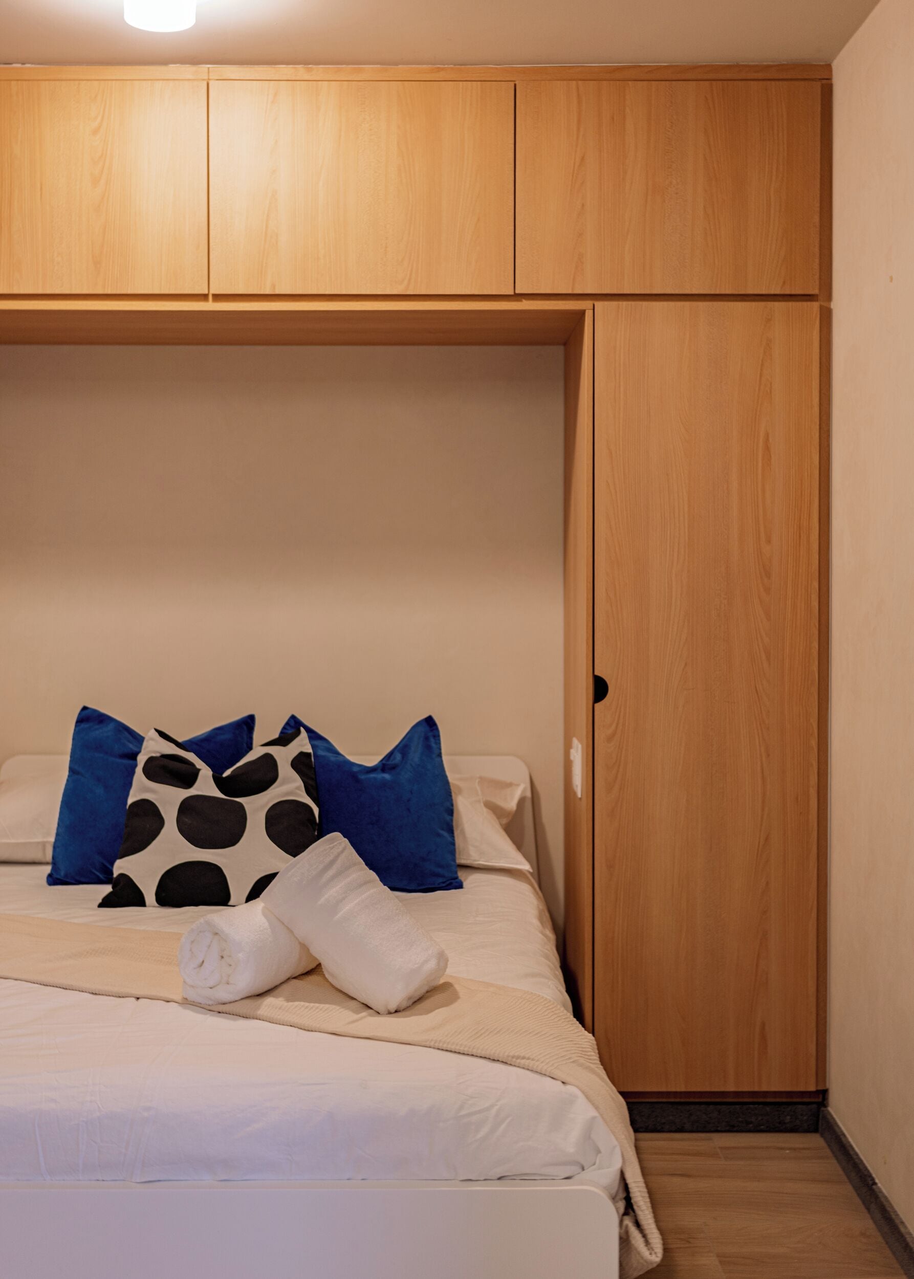 A bedroom with a bed, pillows, a wooden wardrobe, and a light fixture.