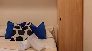 A bedroom with a bed, pillows, a wooden wardrobe, and a light fixture.