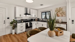 Een moderne keuken met witte kasten, een centraal eiland en een eetgedeelte met een witte tafel.