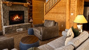 A cozy log cabin interior with a stone fireplace, a Netflix sign, a staircase, and a comfortable seating area. - Luxury Off-Grid Mountain Cabin on 4 Acres, Views, Serenity and Wellness (Jefferson)