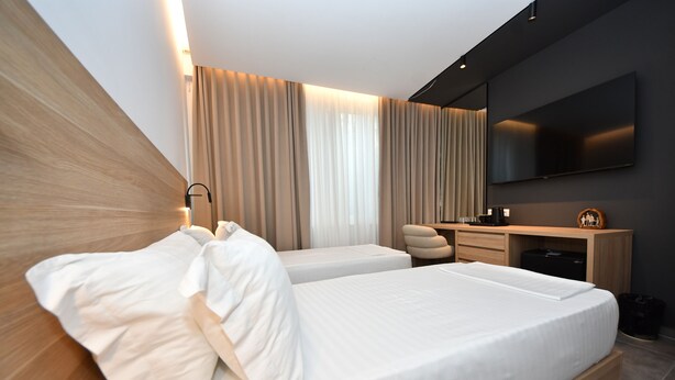 Una habitación de hotel moderna con una cama grande, un escritorio, una silla, un televisor de pantalla plana y un ventanal con cortinas.