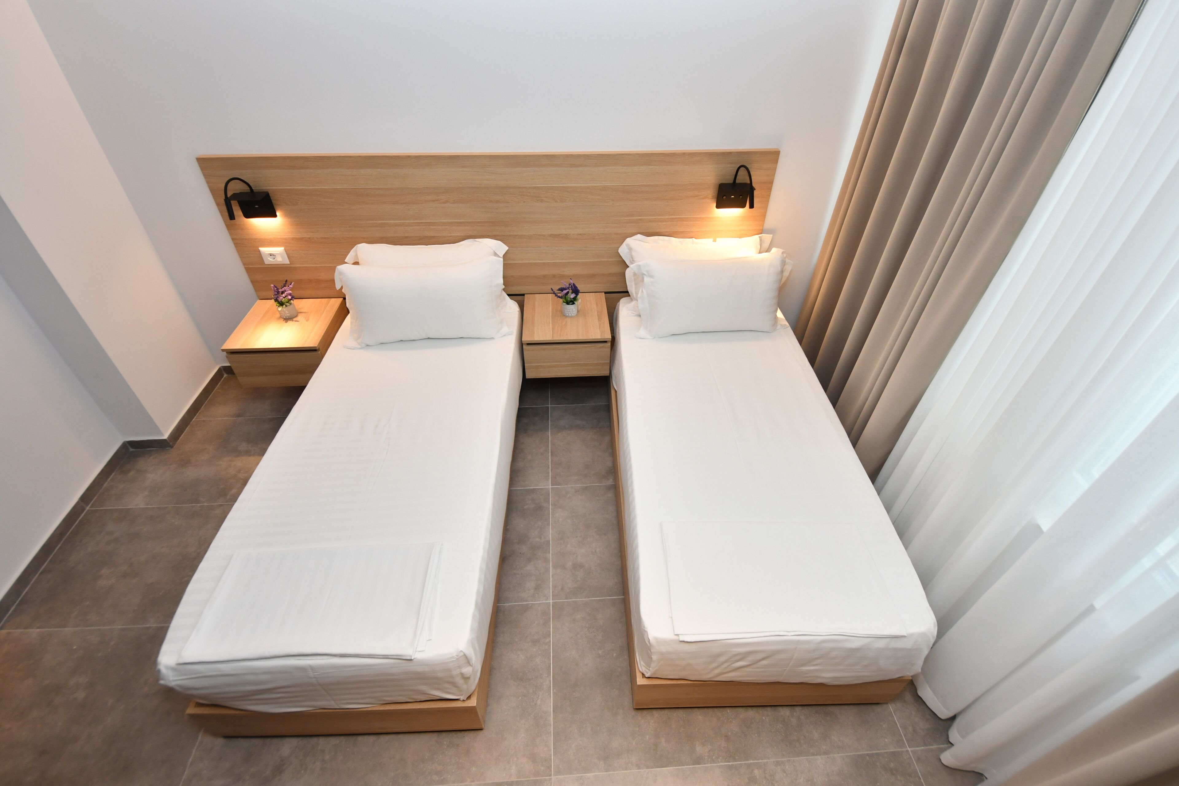 A hotel room with two single beds, wooden headboard, bedside lamps, and a small table with a vase.