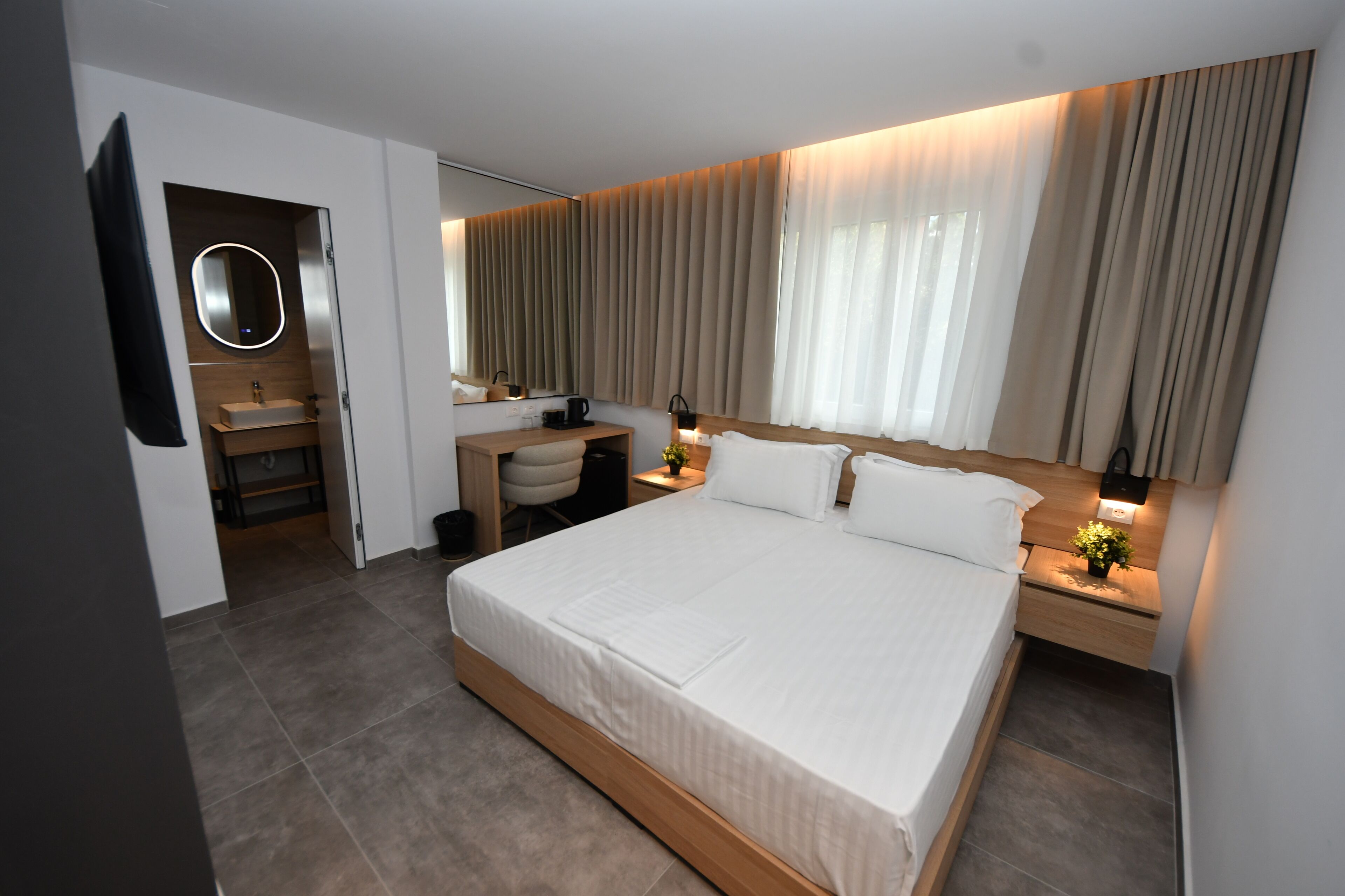 Habitación de hotel moderna con una cama grande, un escritorio con silla, tocador con espejo y televisión montada en la pared.