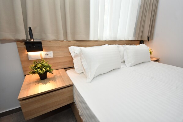 Une chambre d’hôtel avec un lit, une table de chevet agrémentée d’une plante, une prise électrique murale et une prise de courant.