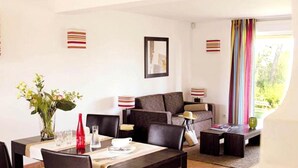 A dining area with a table set for two, a sofa, and a window with curtains. - Golf-side Holiday Home in Mazamet (Roquebrune-sur-Argens)