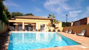 A rectangular swimming pool with clear blue water, surrounded by lounge chairs and umbrellas, and a building with a tiled roof in the background. - Golf-side Holiday Home in Mazamet (Roquebrune-sur-Argens)