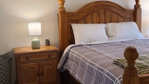 Ein Schlafzimmer mit einem hölzernen Bett, einem Nachttisch mit Lampe, einem gerahmten Bild an der Wand und einem gefliesten Boden.