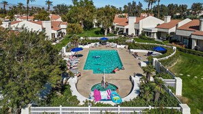 A swimming pool surrounded by white buildings with red-tiled roofs, palm trees, and a white picket fence. - SRC301 Cozy 3BR Santa Rosa Cove Condo near Pool (La Quinta)