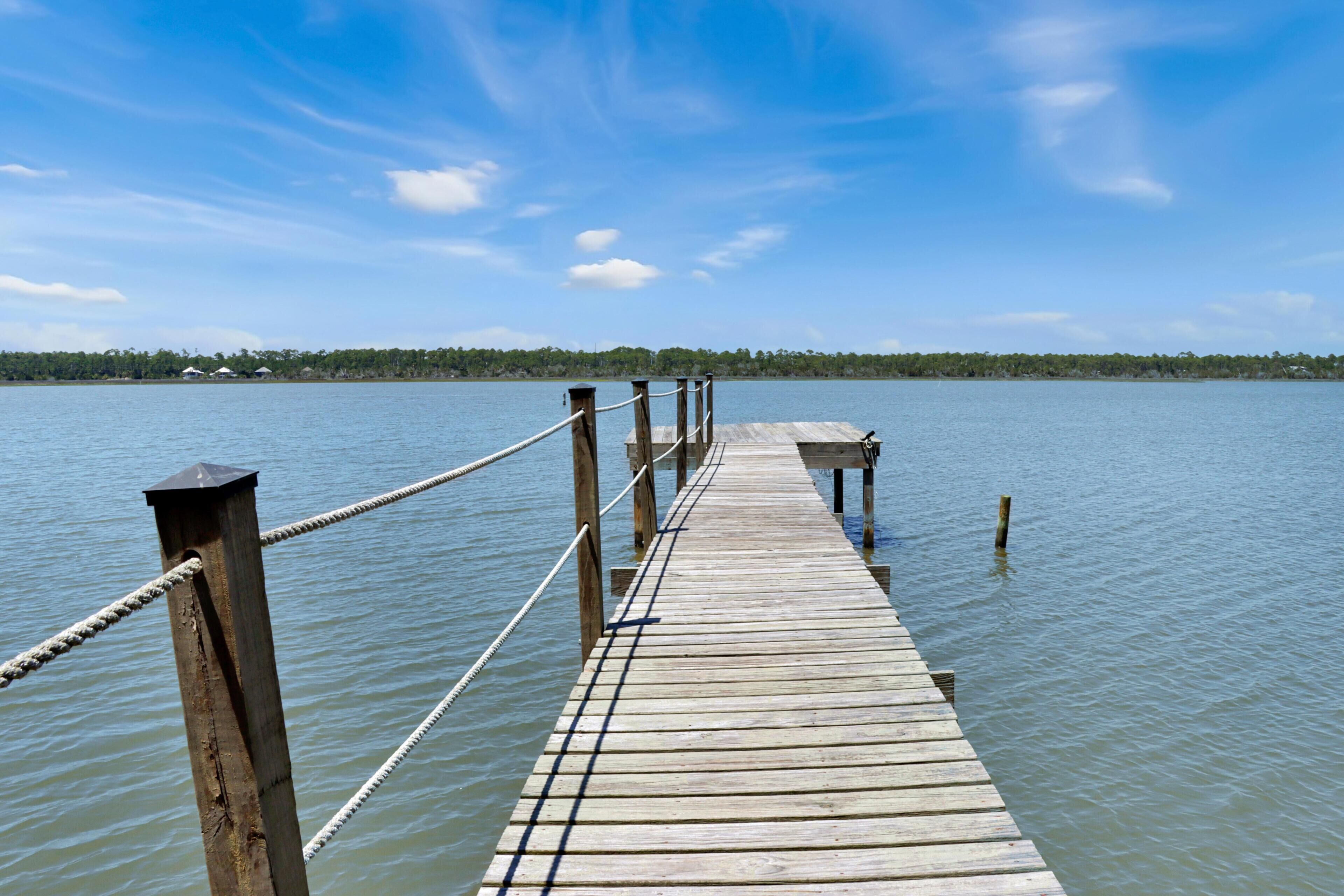 A wooden pier extending into calm water, with a clear sky above.