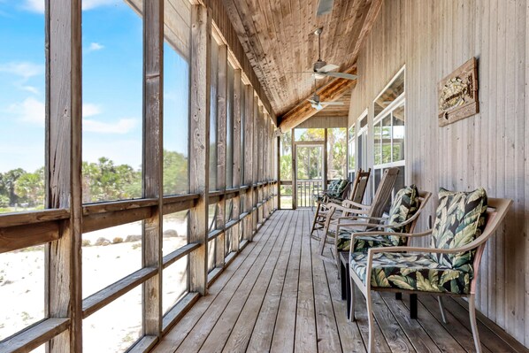 Eine Holzterrasse mit Geländer, Stühlen und einem Deckenventilator.