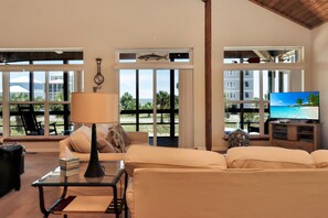Ein Wohnzimmer mit einer Couch, einem Couchtisch, einer Lampe, einem Fernseher und großen Fenstern mit Blick auf Palmen und Gebäude.