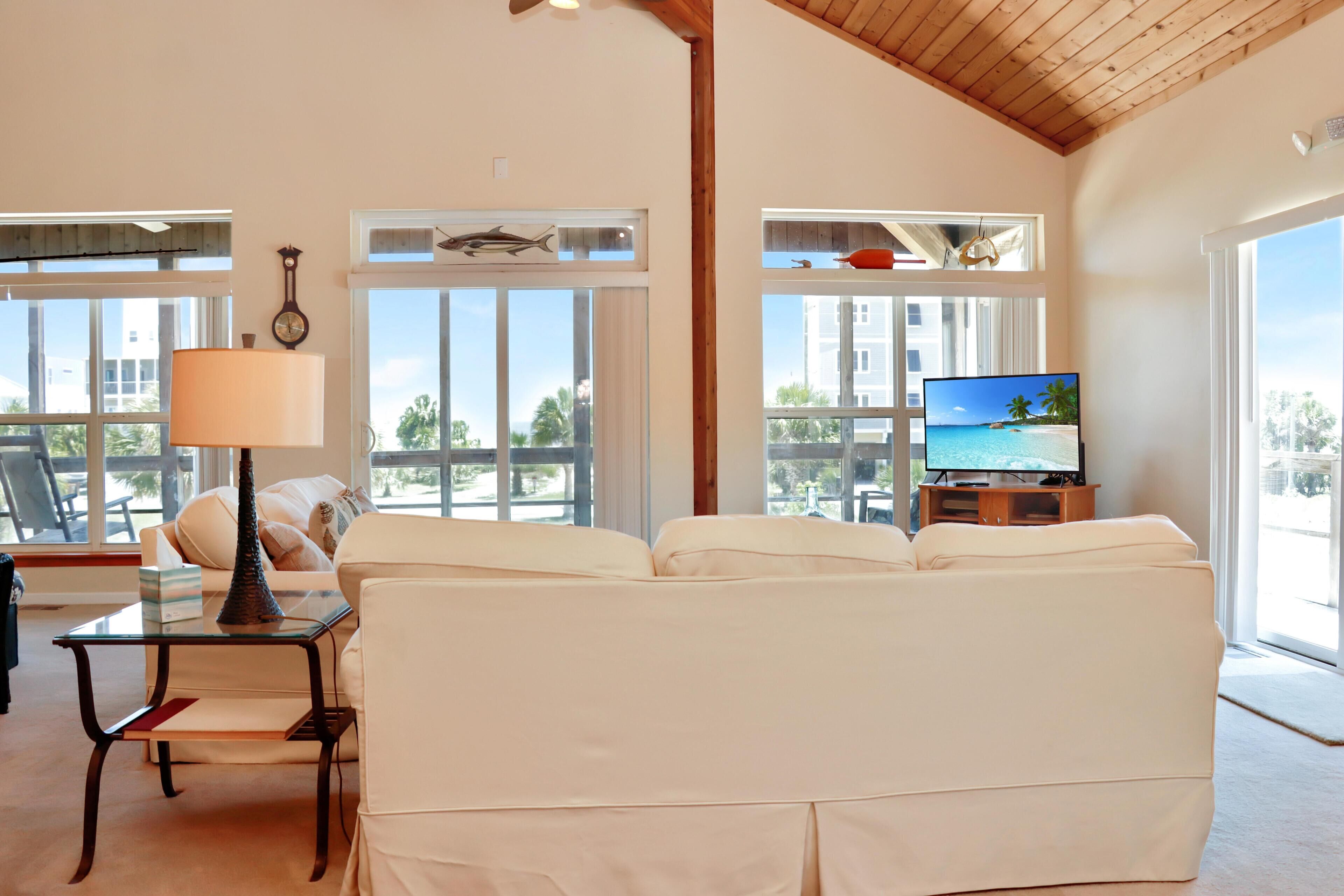 A living room with a sofa, a coffee table, a lamp, a TV, and large windows with a view of palm trees and buildings.