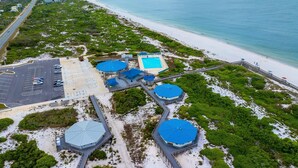 Eine Luftaufnahme eines Küstenresorts mit Schwimmbad, Parkplatz und Strand.