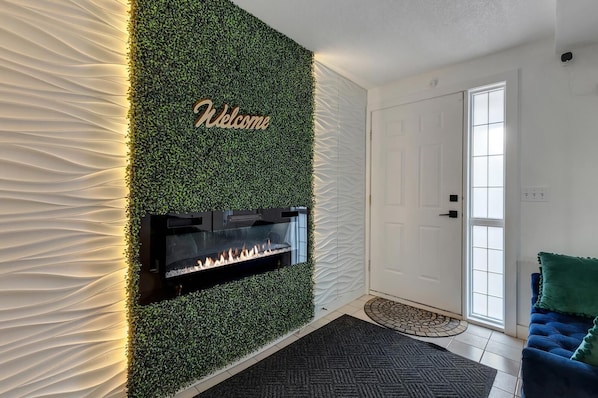 Un salon moderne avec une cheminée, une pancarte « Bienvenue » et une porte.