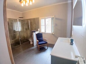 Ein Badezimmer mit Dusche, Toilette, Stuhl und Waschbecken.