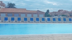 Una piscina con sillas azules, techo de azulejos y edificios al fondo.