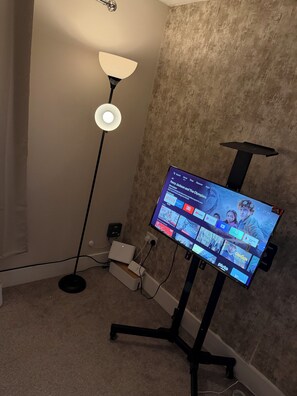 A room with a TV displaying streaming apps, a standing lamp, and a speaker on a carpeted floor. - Room-stylish Double Room & Sofa Bed in S (Gillingham)