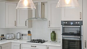 A modern kitchen with white cabinets, a gas stove, an oven, and pendant lights. - Stylish Apartment w/ Parking Near York City Centre (York)
