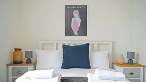 A neatly made bed with white and gray bedding, a blue pillow, and two bedside tables with lamps and decorative items. - Stylish Apartment w/ Parking Near York City Centre (York)