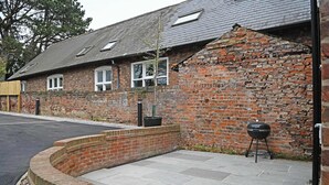 A brick building with a sloped roof, a barbecue grill, and a paved patio area. - Stylish Apartment w/ Parking Near York City Centre (York)
