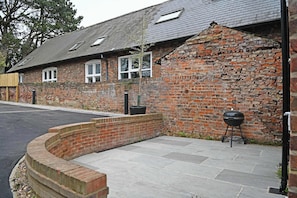 A brick building with a sloped roof, a barbecue grill, and a paved patio area. - The Green - Stylish Home Sleeps 6 with Parking (York)