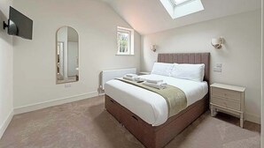 Ein Schlafzimmer mit Bett, Nachttisch, Fernseher, Spiegel, Fenster und Dachfenster.