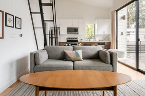Ein modernes Wohnzimmer mit einem grauen Sofa, einem Holztisch und einer Küche im Hintergrund.