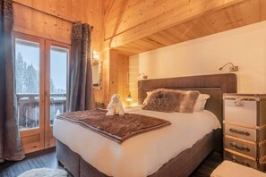Ein Schlafzimmer mit Holzwandverkleidung, einem Bett, einem Nachttisch, einem Koffer und einem Fenster mit Vorhängen.