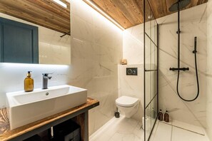 Ein modernes Badezimmer mit einem Holzkosmetikschrank, einem weißen Waschbecken, einer Toilette und einer gläsernen Dusche.