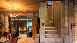 A rustic interior with a wooden staircase, a dining area with a chandelier, and a view through a glass door. - Chalet, 2nd floor, terrace, fireplace or stove, tv, 350m², Combloux (Demi-Quartier)