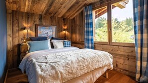 A wooden cabin bedroom with a bed, two bedside lamps, a painting, and a window with curtains. - Chalet, 2nd floor, terrace, fireplace or stove, tv, 350m², Combloux (Demi-Quartier)