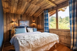 A wooden cabin bedroom with a bed, two bedside lamps, a painting, and a window with curtains. - Chalet, 2nd floor, terrace, fireplace or stove, tv, 350m², Combloux (Demi-Quartier)