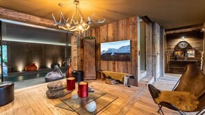 A modern living room with a fireplace, wooden walls, a large TV, and a cozy seating area. - Chalet, 2nd floor, terrace, fireplace or stove, tv, 350m², Combloux (Demi-Quartier)