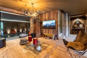 A modern living room with a fireplace, wooden walls, a large TV, and a cozy seating area. - Chalet, 2nd floor, terrace, fireplace or stove, tv, 350m², Combloux (Demi-Quartier)